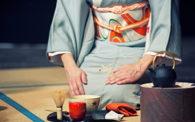 Japanese woman with light blue kimono holding a teacup, during the traditional tea ceremony