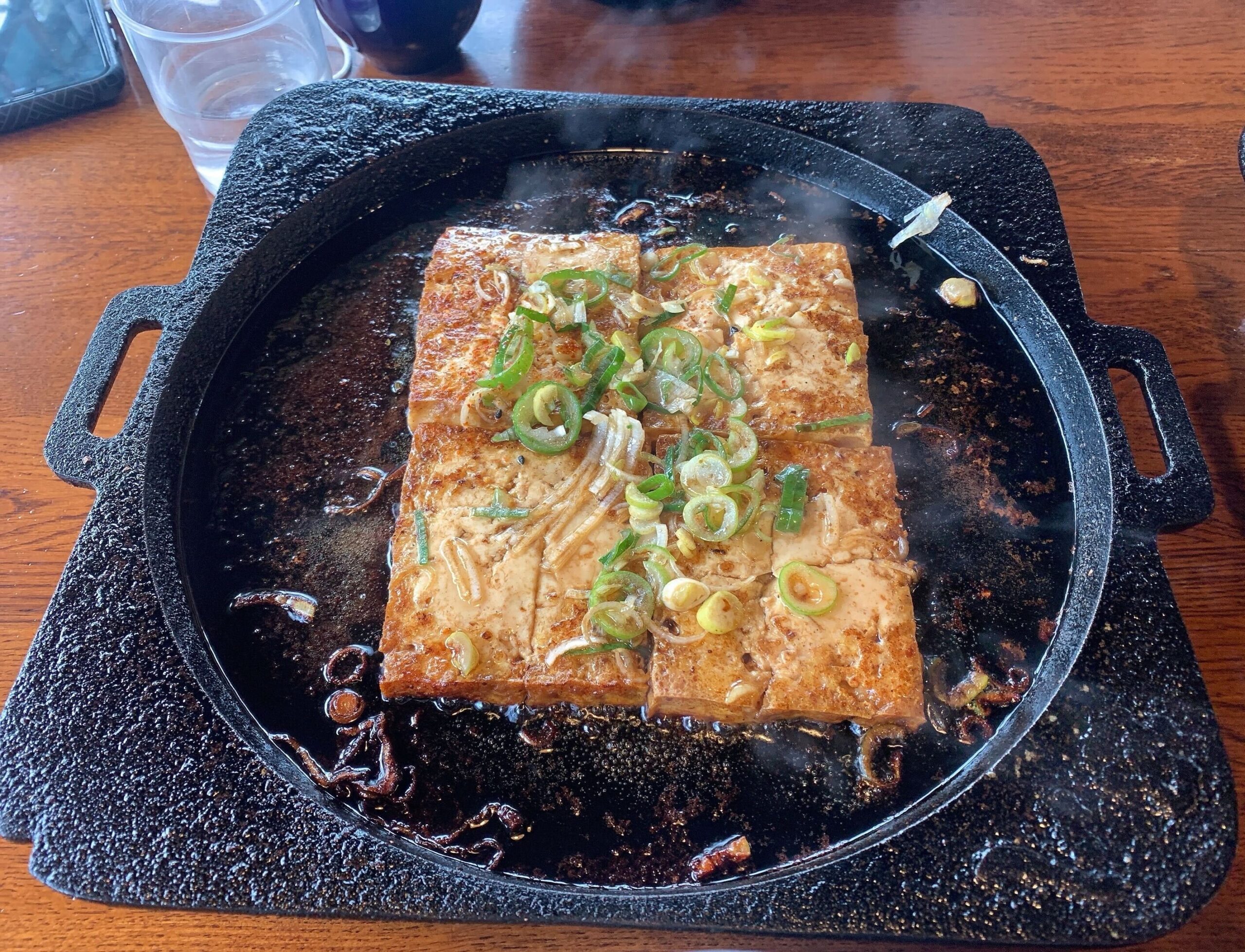 Photo of Takayama's famous tofu steak with green onions on top on a hot iron plate.